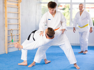 Determined motivated young guy working on martial arts skills in training fight with male rival...