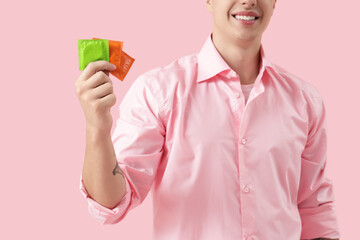 Young man showing condoms on pink background