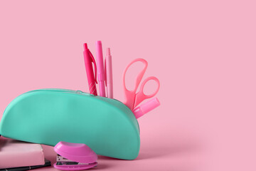 Blue pencil case with different stationery on pink background