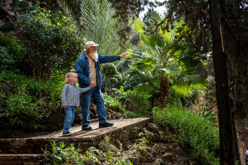 Grandfather pointing to something in the garden while holding his grandson's hand
