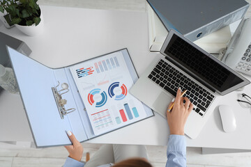 Businesswoman working with laptop and document folder at table in office, top view