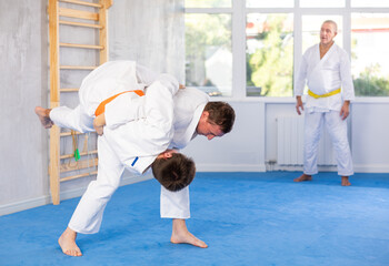 Adult man and young man judokas practicing judo fight in gym..