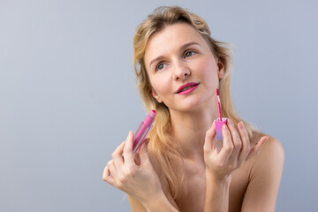 A Beautiful Blonde Woman Holding a Lip Product While Applying Makeup for a Perfect Look on Her Lips...
