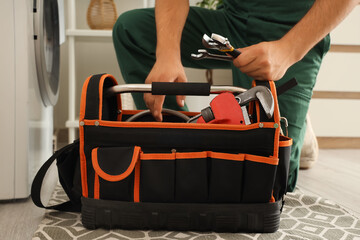 Male plumber with bag of tools fixing washing machine in bathroom, closeup