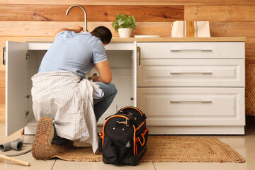 Male plumber fixing sink in kitchen, back view