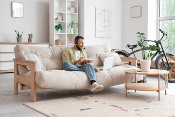 Freelancer with headset using laptop and doing notes at home
