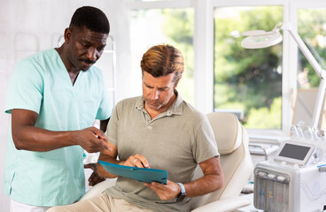 African man doctor shows clinic man client papers for familiarization and signing of consent for...