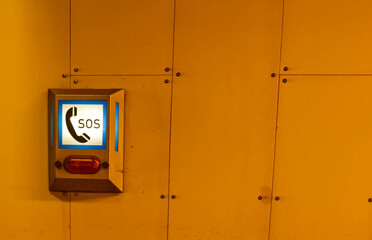 An emergency SOS call box mounted on a wall, illuminated with blue light. The box features a phone...