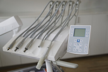 A close-up view of a dental chair control panel with multiple hoses and a digital display, set in a modern dental clinic environment.