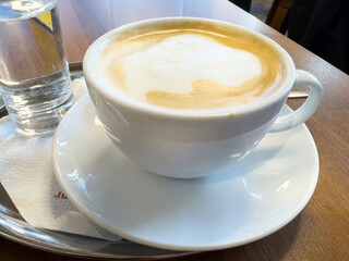 Creamy cappuccino in white cup on wooden table with glass of water