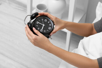 Female hand with black alarm clock in bedroom