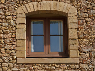 Rustic Window's Charm: A classic window set in a weathered stone wall, framed with an elegant arched sandstone surround, offering a glimpse into the beauty of traditional architecture.
