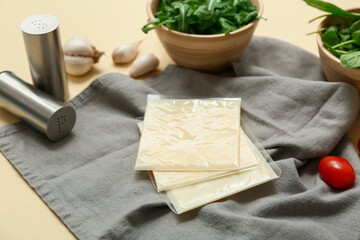 Napkin with slices of tasty processed cheese, garlic and pepper shaker on beige background. Closeup