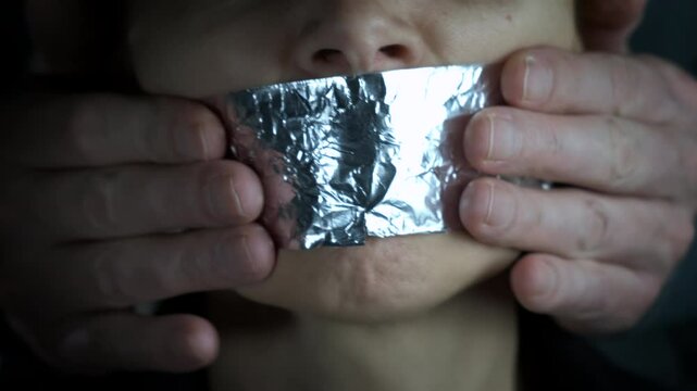 Aggressive man put tape on mouth. A view of female with aggression put the tape on the female mouth on the black background.