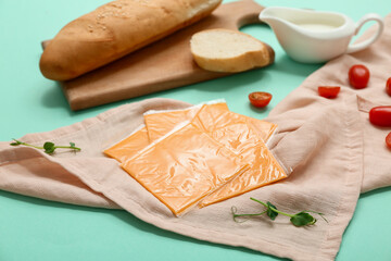 Slices of tasty processed cheese, tomatoes and board with bread on turquoise background. Closeup