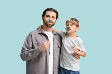 Dad and little son with paper mustache on blue background. Father's day