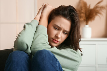Depressed young woman sitting in armchair in living room. Closeup