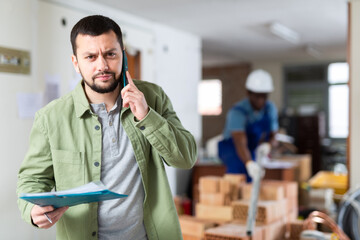 Portrait of irritated young man architect emotionally talking on phone at indoor building...