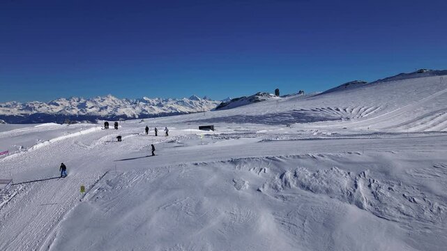 Panoramic view of the snow-covered Alpine mountains on a sunny, cloudless day, with skiers passing by on Glacier 3000 and a backdrop of Quille du Diable.