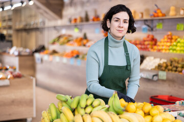 While working in shop, employee forms display case, puts ripe imported lemon in pile. Open display of goods in self-service shop. Female employee makes attractive display case with vegetables.