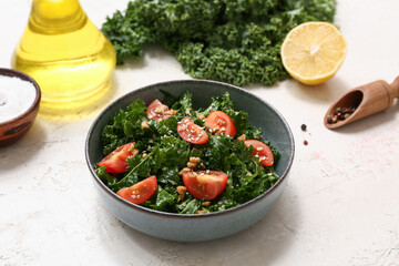 Composition with bowl of tasty kale salad, spices and oil on light background