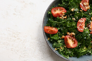 Bowl of tasty kale salad with tomatoes and walnuts on light background