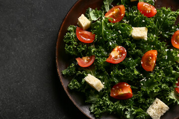 Plate of tasty kale salad with croutons and tomatoes on dark background, closeup