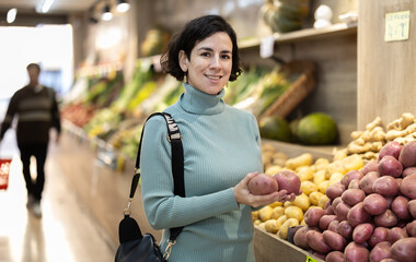 European woman stands in a vegetable pot and chooses potatoes. Shopper looking at sweet potatoes in supermarket