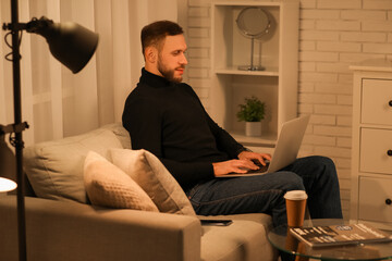 Young freelancer using laptop on sofa at home in evening