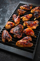 Traditional barbecue chicken wings, drumsticks and chicken breast with hot chili sauce served as closeup on a rustic grill grate