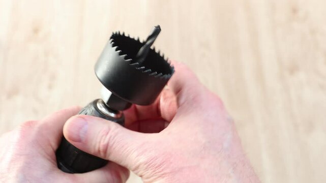Spade bit attached to cordless screwdriver is making opening for door latch, and tip of bit appears in larger hole.