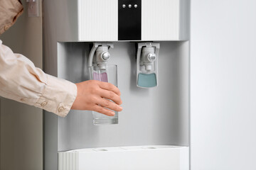 Female hands pouring water from cooler on light background