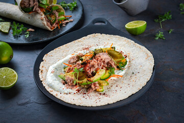 Italian style wrap piada wheat tortilla with tuna fish, vegetable and avocado served as closeup on a Nordic design plate