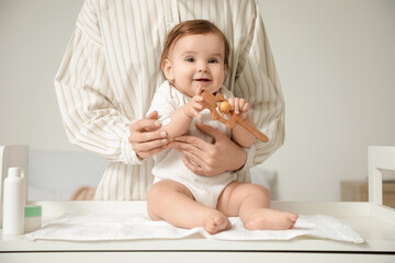 Mother applying cream on her little baby's arm on changing table in room. Closeup