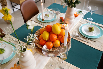 Beautiful table setting with citrus fruits and candle on green tablecloth in living room. Closeup
