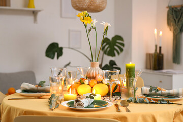 Festive table setting with citrus fruits, flowers and burning candles in room. Closeup