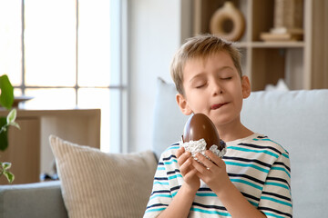 Little boy licking his lips and holding chocolate egg in living room