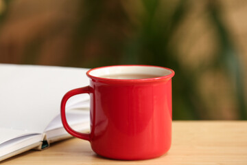 Red mug of black tea on wooden table on blurred background. Closeup
