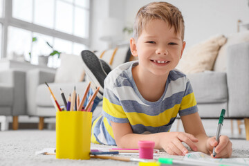 Smiling little boy drawing with felt-tip pens on floor at home