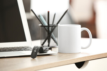 White ceramic mug on table near laptop and wrist watch in office