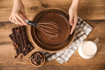 Woman stirring delicious chocolate sauce in bowl with whisk on table in kitchen. Top view