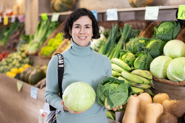 Fototapeta premium Woman pulls cabbage in his hands and chooses which one to cook soup and salad. Female customer came to a supermarket for fresh vegetables