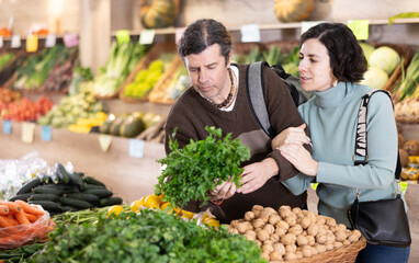Couple adult man and woman buyers chooses bunch of parsley in vegetable shop