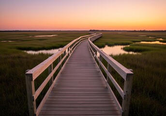 Obraz premium A serene boardwalk leads through a marshland at sunset, reflecting golden hues on calm waters.