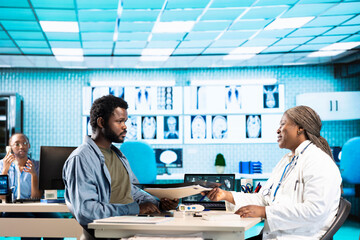 Medic takes notes during routine checkup visit with young man, reviewing his healthcare records and recommending the best treatment for disease prevention. Healthcare industry.