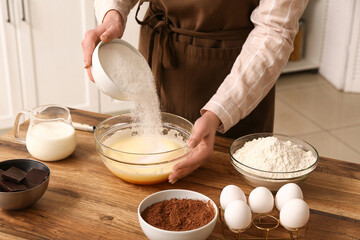 Woman adding sugar into bowl with dough at table in kitchen. Closeup