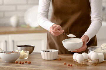 Woman preparing chocolate brownie with spoon of sugar at table in kitchen. Closeup