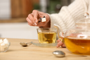 Woman putting lump of sugar into tea at table in kitchen. Closeup