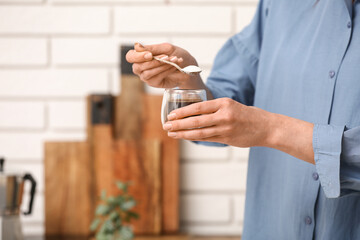 Woman adding spoon of sugar into cup of coffee in kitchen. Closeup