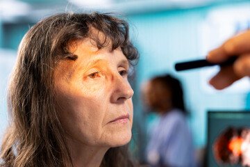 Ophthalmologist conducts eye exam for a senior woman in cabinet. Healthcare provider using modern optical equipment for vision correction, eyesight diagnostics in a medical office. Close up.